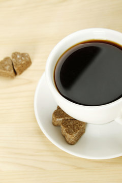 Closeup of a white cup of coffee next to lay pieces of sugar