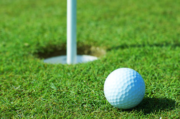 Golf ball on green grass in front of hole