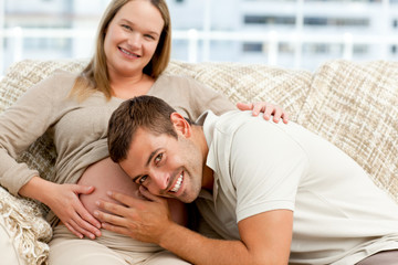 Smiling future dad listening to the belly of his wife sitting on