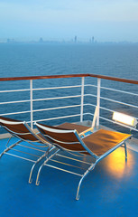 Two illuminated  deck-chair on ship deck overlooking city