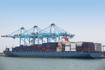 Big cargo boat docked to industrial port with several blue crane