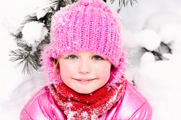 Little girl in winter pink hat in snow forest.