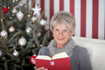 Obraz na płótnie Canvas moderne seniorin liest vor dem weihnachtsbaum