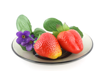 Artificial flowers and strawberries on saucer.