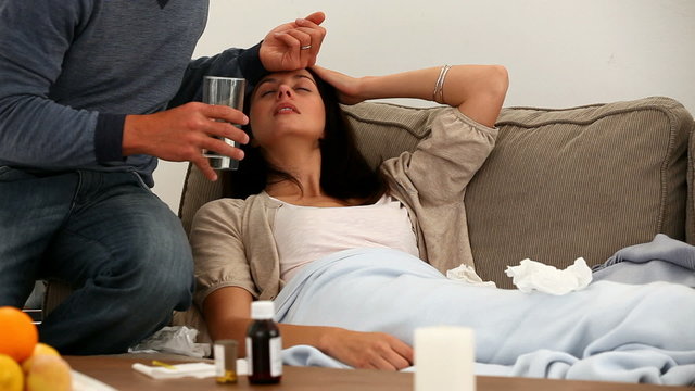 Man giving pills to his sick wife on the sofa
