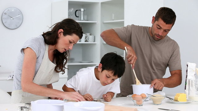 Cute boy making biscuits with his parents in the kitchen