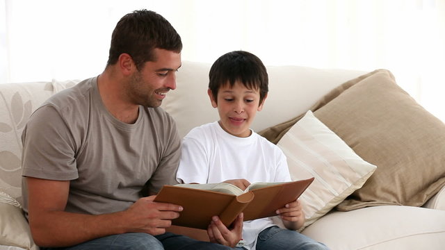 Father and son looking at a book on the sofa