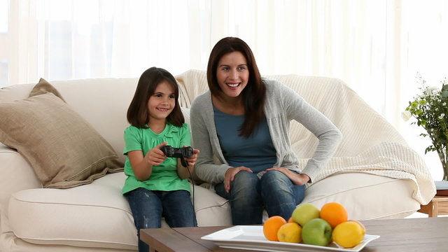 Proud mom encouraging her daughter playing video games at home