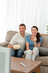 Cute couple eating pop corn while watching television on sofa