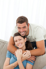 Fototapeta premium Happy man hugging his girlfriend sitting on the sofa
