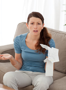 Worried woman misunderstanding her bills sitting on sofa