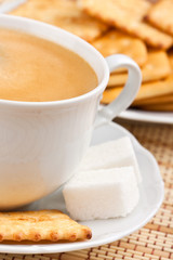 A cup of coffee with a lump sugar and crackers for breakfast