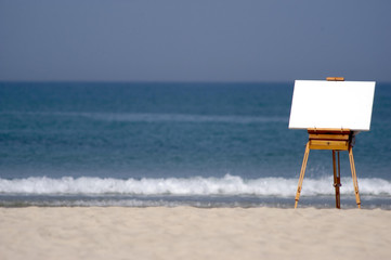 A blank canvas rests on a wooden easel on a beach