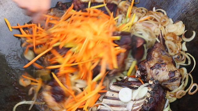 Adding carrots to kettle with cooking meat, closeup.
