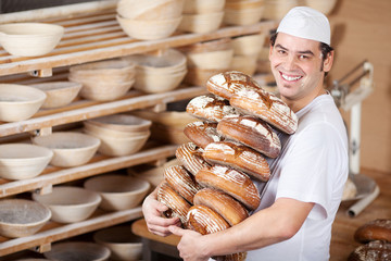 lachender bäcker mit broten in der backstube