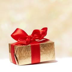Golden gift box with red bow on blurred background