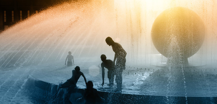 Children silhouettes playing in water fountain at sunset