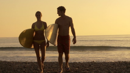 Young couple walking with surfboards on beach at sunset