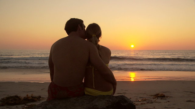 Back side of young couple kissing on beach at sunset