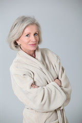 Senior woman in bathrobe standing on white background