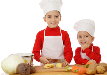 Smiling little chief-cookers on the desk with vegetables