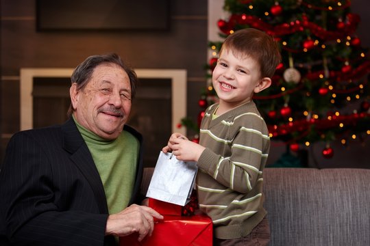 Young boy giving christmas present to grandfather