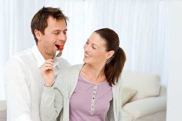 Happy man tasting a tomato while his girlfriend preparing lunch