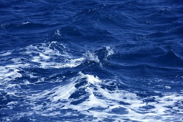 Fototapeta na wymiar Blue wawy water with white foam in storme sea ocean surface