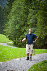 active handsome senior man nordic walking outdoors on a forest p