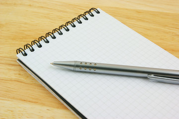 Pen and blank note pad on wooden background