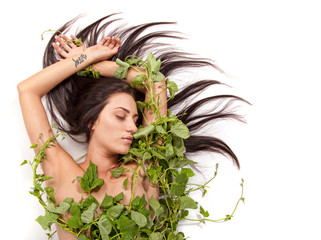 Young beautiful nude woman with green ivy leaves wrapped around