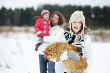 Happy family and a cat having fun on beautiful snowy winter day