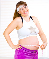 Laughing  beautiful pregnant female measuring  belly.