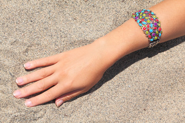 closeup of womans hand with multicolored bracelet on sand, sunny