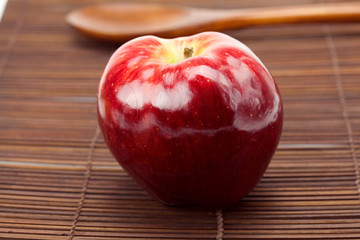 red apple and a wooden spoon on a bamboo mat