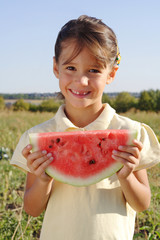 Smiling little girl with slice of watermelon on field