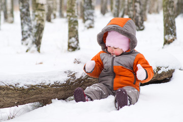 Fototapeta na wymiar cute baby sit on snow in park and play with mittens