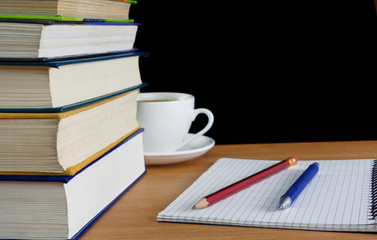 pen and pencil on notebook near pile of books on table