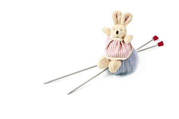 Toy doe rabbit sitting on mohair clew with knitting needles