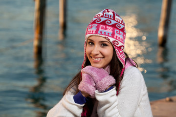 Pretty young woman in winter clothing along the bay at sunset