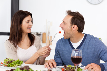 Pretty woman giving a tomato to her boyfriend while having lunch