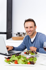 Fototapeta na wymiar Cheerful man working on his laptop while having lunch