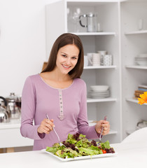 Obraz na płótnie Canvas Pretty woman preparing a salad standing in the kitchen