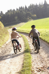 Two young children ride bicycles in park