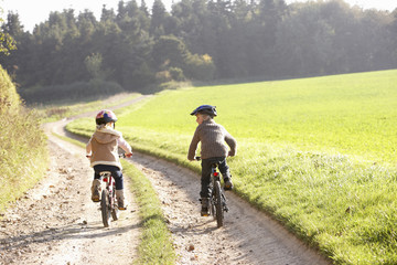 Fototapeta premium Two young children ride bicycles in park