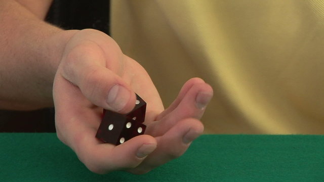 Hands rolling a pair of dice on a poker table