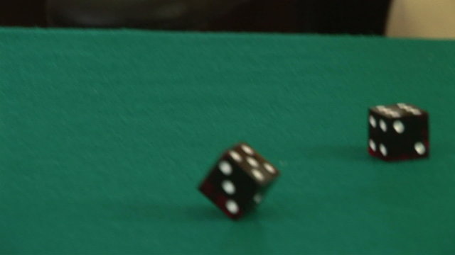 Hands rolling a pair of dice on a poker table