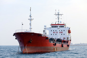 Red tanker is at anchor near the port.