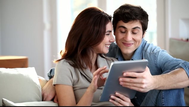 Couple sitting in sofa with electronic pad