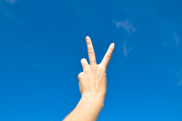 Victory gesture against blue sky